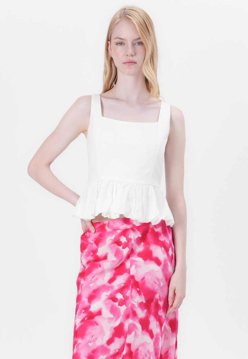 Haut peplum blanc avec un décolleté carré, porté sur une jupe à motif abstrait rose et blanche. Texture de tissu lisse, corsage ajusté.