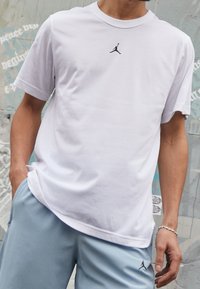 Vit bomull t-shirt med korta ärmar och rundad halsringning, med en liten svart Air Jordan-logga på bröstet.