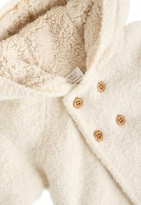 Kreemja värviga beebimantel, millel on pehme tekstuur, voodriga kapuuts ja puidust nööbid. Pehme materjal pakub soojust ja mugavust.