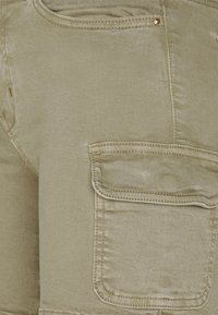 Pantalones cortos de algodón verde oliva con acabado texturizado, bolsillo trasero con tapa y detalles de costura en contraste.