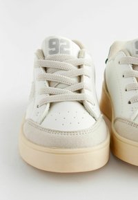 Baskets en cuir blanc avec des accents en daim beige, bout rond, profil bas, lacets texturés et un logo argenté 92 sur la languette.