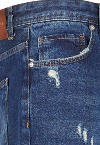 Jeans de mezclilla de color azul oscuro, con detalles desgastados y una etiqueta de cuero en la cintura. Presenta bolsillos frontales y costuras en contraste.