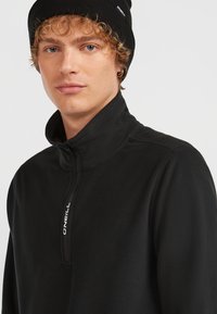 Sort fleece pullover med høj krave, lynlåse bryst, og broderet logo. Stoffet har en blød tekstur og en afslappet pasform.