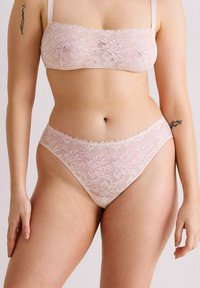 Bralette en dentelle et culotte taille haute assortie en rose clair, ornée de motifs floraux et de bords festonnés. Texture douce et délicate.