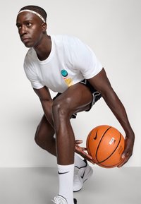 Bílý tričko s grafikou basketbalového míče, černé šortky, tenisky Nike a oranžový basketbal. Hladká látka, sportovní design a živé barvy.