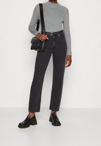 Jeans negros de tiro alto y pierna recta combinados con una blusa de manga larga de canalé gris; acompañados de unos mocasines negros de tacón cuadrado y un bolso negro texturizado.