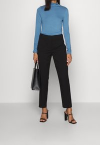 Ljusblå polo, åtsittande, långärmad; högmidjade svarta skräddarsydda byxor; svart handväska; svarta sandals.