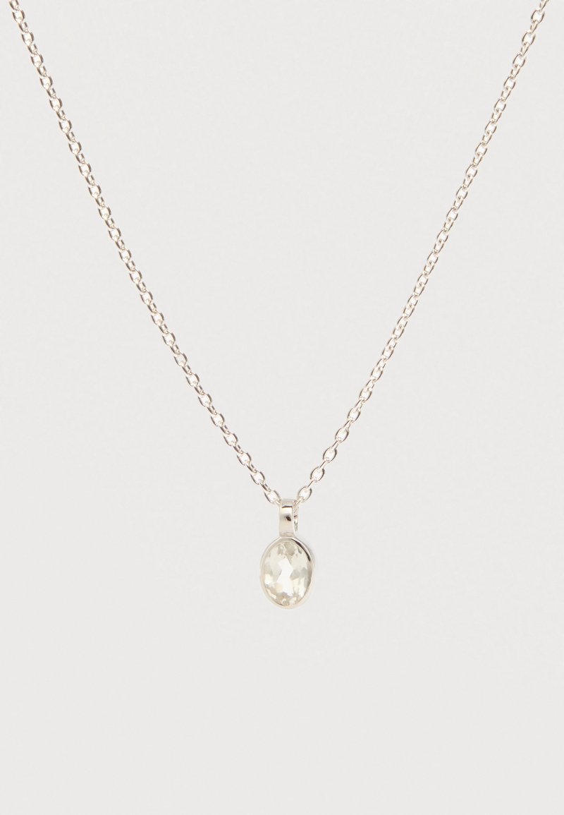 Stříbrný řetízek s malým oválným přívěskem z čirého broušeného kamene na světlém pozadí.