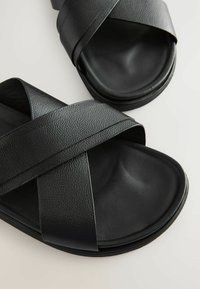 Sandales noires à brides croisées en matériau synthétique texturé, avec un design de brides larges et une semelle intérieure rembourrée.