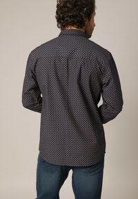 Lange mouwen shirt met een marineblauwe stof met een klein geometrisch patroon. Klassieke kraag en rechte zoom. Gelaagde afwerking voor extra detail.