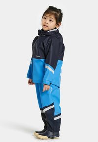 Blå och marinblå vattentät regnoverall med kontrasterande randiga detaljer. Har huva och elastiska muddar; tillsammans med svarta gummistövlar.