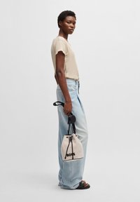 Lys beige kortærmet top, højtaljede falmede blå jeans, og en creme bucket bag med sorte detaljer holdt i hånden.