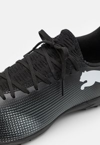 Zapatilla deportiva negra con parte superior texturizada, que presenta cordones y un logo blanco. Acabado suave con un patrón de rejilla y un diseño aerodinámico.