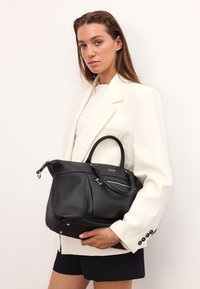 Fekete bőr kézitáska texturált felülettel, két felső fogantyúval és egy cipzáras zsebbel. Kiegészítők közé tartozik a fém hardware és a márka logó.