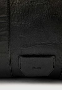 Black leather bag featuring a textured surface, prominent stitching, and a small embossed label. The shape is rectangular with angled edges.