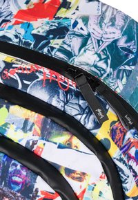 Plecak z wielokolorowego płótna z abstrakcyjnymi wzorami graffiti, czarnymi zamkami błyskawicznymi i akcentami, gładką fakturą oraz wieloma zasuwanymi przegrodami.