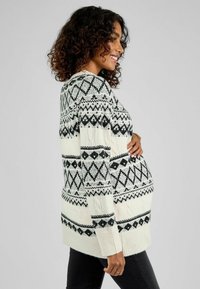 Gestrickter Schwangerschaftspullover in Schwarz und Weiß, mit geometrischen Mustern, langen Ärmeln und gerippten Bündchen. Lockere Passform für hohen Tragekomfort.