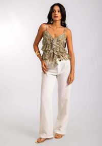 Top de tirantes finos con estampado floral y volantes en beige y oliva, combinado con pantalones de lino blancos de pierna ancha y sandalias minimalistas.