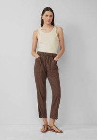 Débardeur côtelé crème et pantalon marron à taille élastique avec poches, présentant une coupe décontractée et des jambes fuselées. Sandales beiges avec des lanières à imprimé léopard.