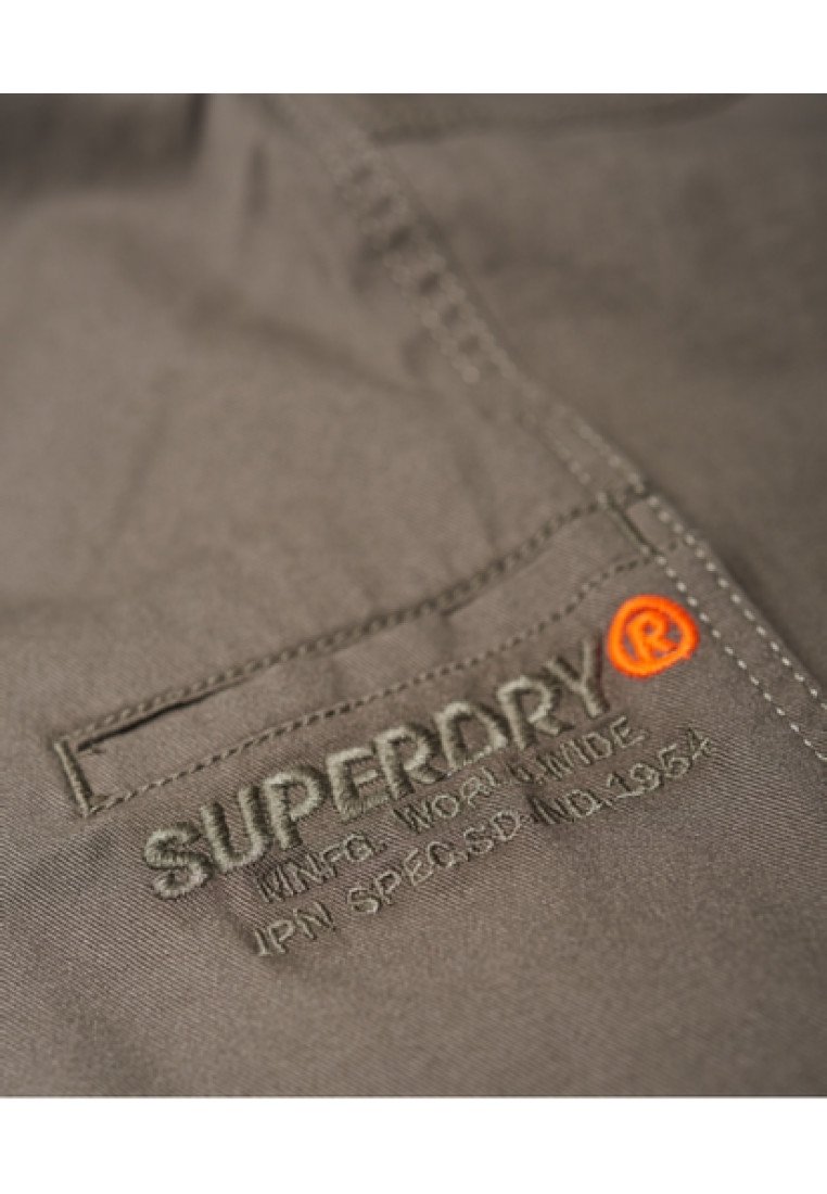 Närbild av grått tyg med sydd ficka och broderat "SUPERDRY" varumärke och logotyp i orange och grå tråd.