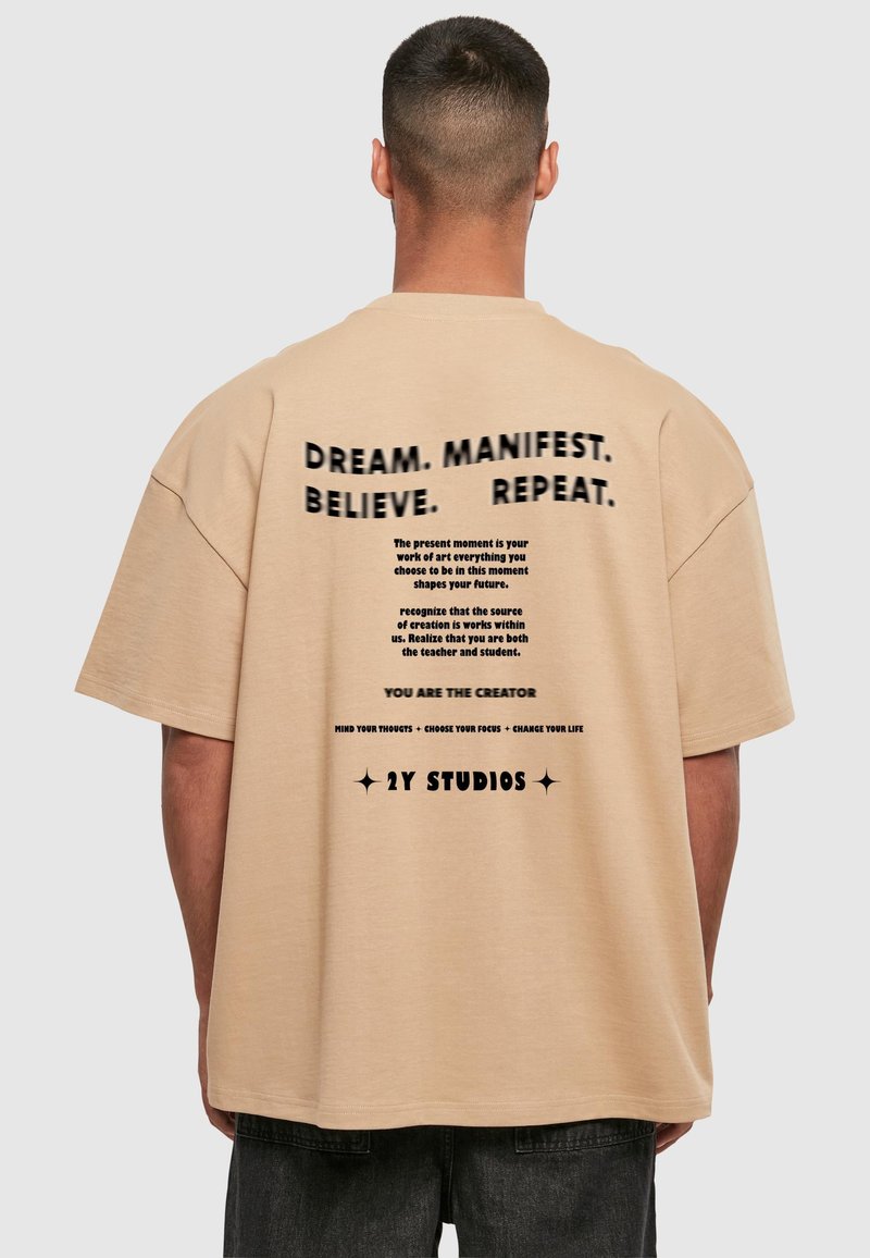 Beige oversized t-shirt med svart text på baksidan som har motiverande fraser och varumärke från 2Y Studios. Rund hals och korta ärmar.