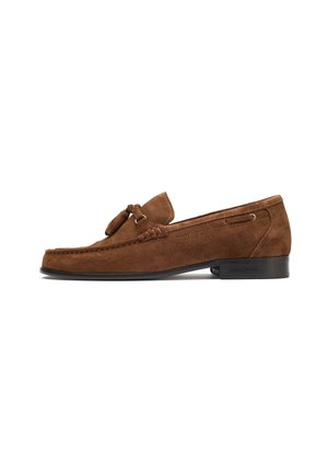 Brown suede loafers with a flat rubber sole, featuring a decorative bow at the front and woven detail along the vamp.