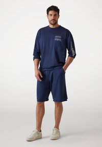 Marineblauw sporttop met een mesh-structuur en de opdruk "ATHL. DEPT.", gecombineerd met bijpassende shorts en witte sneakers.