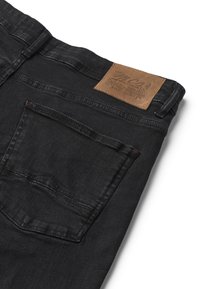 Blugi negri din denim pliați pentru a arăta buzunarul din spate și eticheta maro din piele a brandului cusută pe talie.