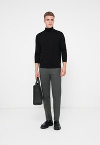 Pulover negru cu guler înalt, ajustat. Pantaloni gri, cambrati, cu o textură subtilă. Geantă din piele neagră. Pantofi negri masivi. Fundal simplu.