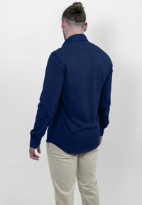 Donkerblauw overhemd met lange mouwen, een reguliere kraag, een getailleerde pasvorm en knoopmanchetten. Gemaakt van gladde stof en heeft een gebogen zoom.