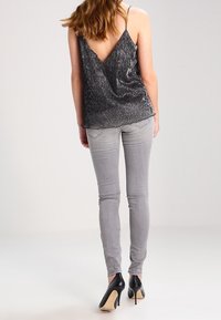 Camiseta de tirantes metálica negra con un profundo escote en la espalda, combinada con jeans ajustados gris claro y tacones negros de charol. Textura suave, diseño ajustado.