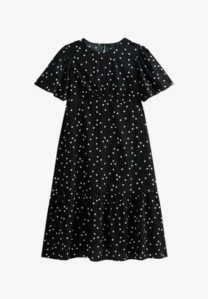 Czarna sukienka w białe kropki, krótki bufiaste rękawy, marszczony dekolt i warstwowa spódnica. Wykonana z gładkiego materiału o delikatnym połysku.
