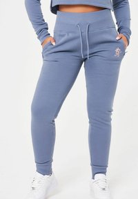 Ljusblå, åtsittande joggarbyxor i mjukt material med elastisk midja och dragsko. Har sidofickor och broderidetaljer.