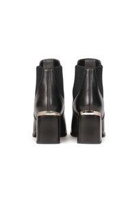 Botas de tobillo negras de cuero y textil, con tacón de bloque y acentos metálicos, paneles laterales elásticos y una textura suave.