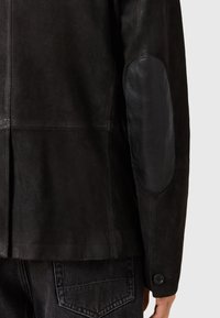 Chaqueta de cuero negra con una textura suave y un parche de cuero en el codo en contraste. Incluye un botón en el puño y un diseño minimalista.