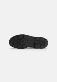 Black rubber shoe sole with distinctive tread pattern, featuring angular lugs and deep grooves for grip. Smooth, flat surface at the heel.