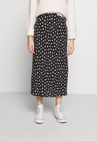 Black midi skirt with a scattered pattern of light beige and white shapes, made of lightweight fabric; paired with white sneakers.