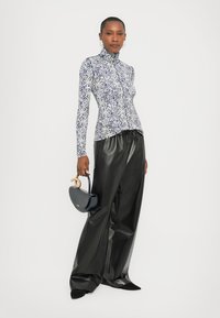 Fitted turtleneck top with a blue and white floral pattern, paired with loose black leather pants. Small black handbag with a gold accent.