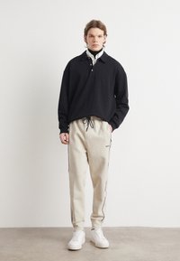 Sort langærmet polo med krave, parret med beige sweatpants med snor, der har sorte sidestriber og hvide sneakers.