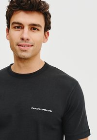 Czarna bawełniana koszulka z okrągłym dekoltem i krótkimi rękawami, z małym białym haftowanym logo na lewej piersi.