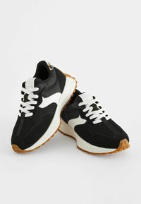 Des chaussures de sport noires avec des accents et des lacets blancs, présentant un mélange de matériaux en daim et en maille, ainsi qu'une semelle extérieure en caoutchouc avec un design texturé.