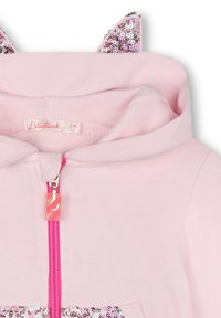 Felpa rosa con zip completa, con orecchie decorate con paillettes. Tessuto morbido, tasca a marsupio e una zip rosa luminosa con un tirante decorativo.