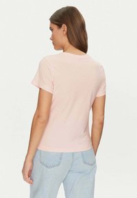 T-shirt rosa a maniche corte realizzato in morbido cotone, con un classico collo a giro, una texture liscia e una forma aderente. Indossato con jeans azzurri chiari.