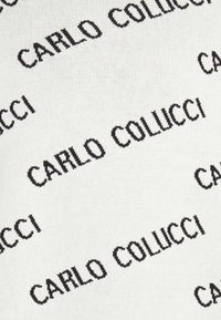 Strickstoff mit einem weißen Hintergrund, auf dem wiederholt schwarzer Text in einer fett gedruckten Serifenschrift mit der Aufschrift "CARLO COLUCCI" zu sehen ist.