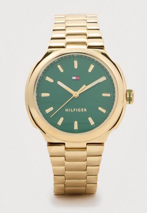 Zlatni metalni ručni sat s zelenim brojčanikom, zlatnim oznakama sati i kazaljkama, logotipom Tommy Hilfiger i povezom za narukvicu.