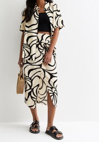 Zwart-wit bloemenpatroon korte mouwen shirt gedragen met een geknoopt rokje, aangevuld met zwarte sandalen en een geweven tas.