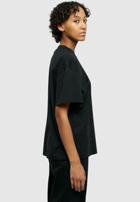 T-shirt en coton noir à manches courtes, coupe décontractée, col rond et minimalisme au niveau de la marque sur le devant. Texture lisse, design décontracté.