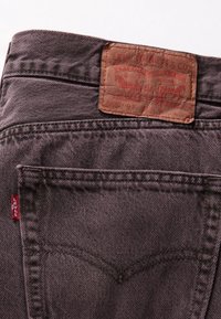 Jeans de mezclilla gris oscuro con un parche de cuero con una marca en relieve. Costuras visibles y diseño del bolsillo trasero con un detalle de etiqueta roja.
