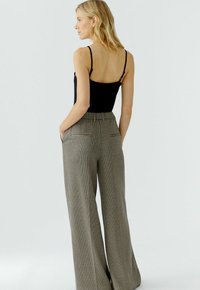 Schwarzer ärmelloser Bodysuit kombiniert mit hochgeschnittenen, weiten Karo-Hosen mit Hahnentrittmuster und Gesäßtaschen.