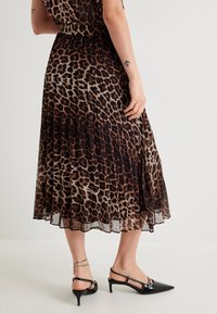Abito leopardato nero e marrone con texture plissettata, orlo fino al ginocchio, abbinato a tacchi a punta neri.